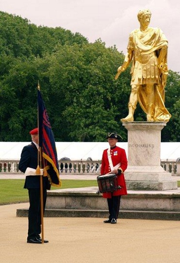 A picture of the standard bearer and drummer stood in front of the statue of King Charle 2nd as a roman leader
